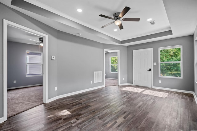 interior space featuring visible vents, dark wood-type flooring, a raised ceiling, and a ceiling fan