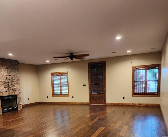 unfurnished living room featuring dark wood-style floors, baseboards, a stone fireplace, and ceiling fan