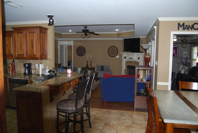 kitchen featuring a ceiling fan, a peninsula, a sink, dishwasher, and a kitchen breakfast bar