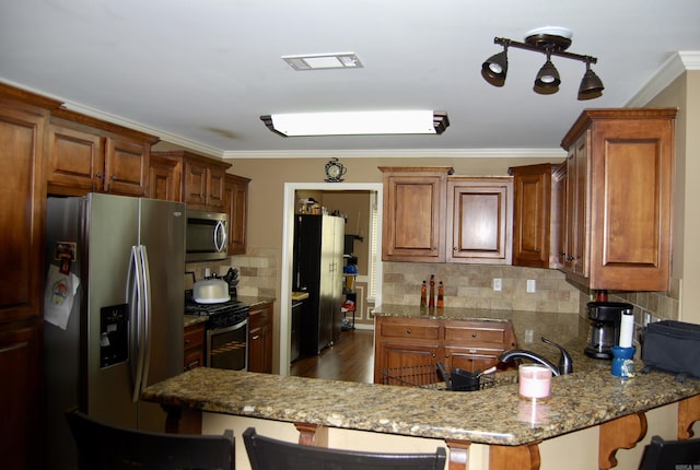 kitchen with a breakfast bar, ornamental molding, stone countertops, a peninsula, and appliances with stainless steel finishes