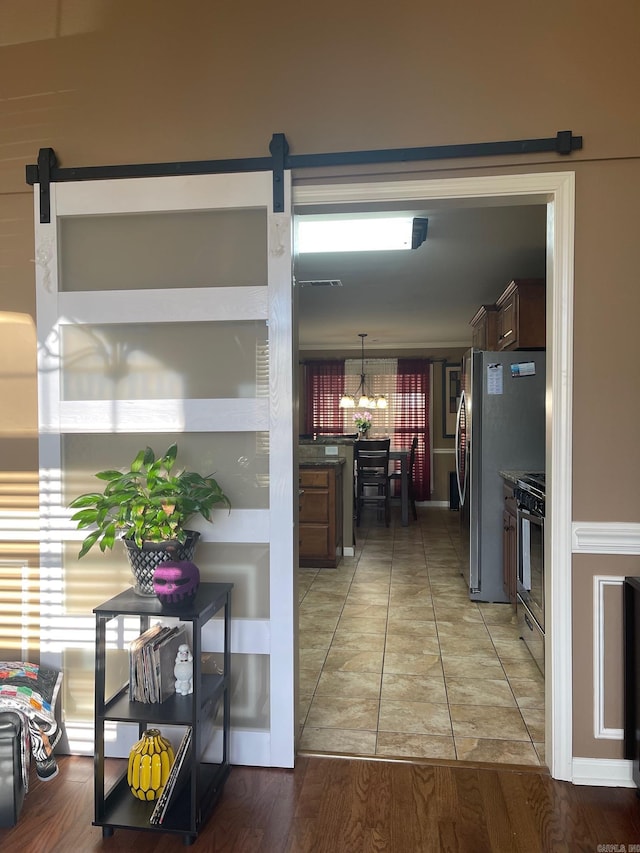 kitchen featuring light wood-style flooring, freestanding refrigerator, range with gas cooktop, a barn door, and a notable chandelier