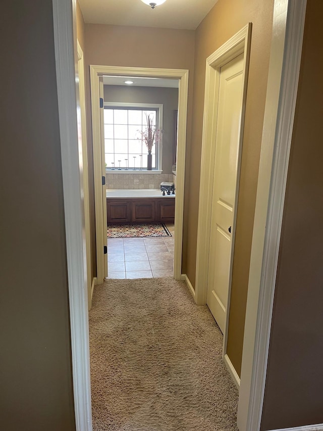 hall featuring light tile patterned floors, baseboards, and light carpet