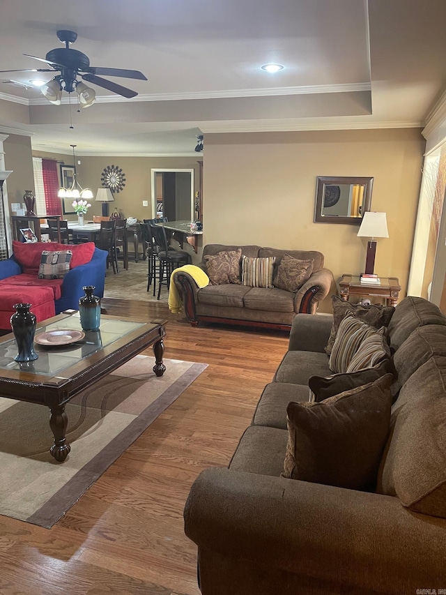 living area with wood finished floors, a raised ceiling, ceiling fan, and ornamental molding