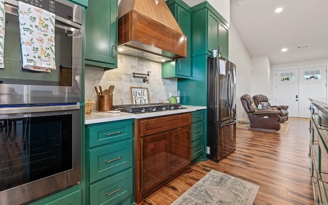 kitchen featuring light wood-type flooring, appliances with stainless steel finishes, light countertops, green cabinetry, and custom exhaust hood