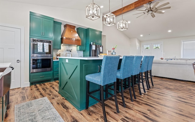 kitchen with green cabinets, light countertops, custom range hood, appliances with stainless steel finishes, and wood finished floors