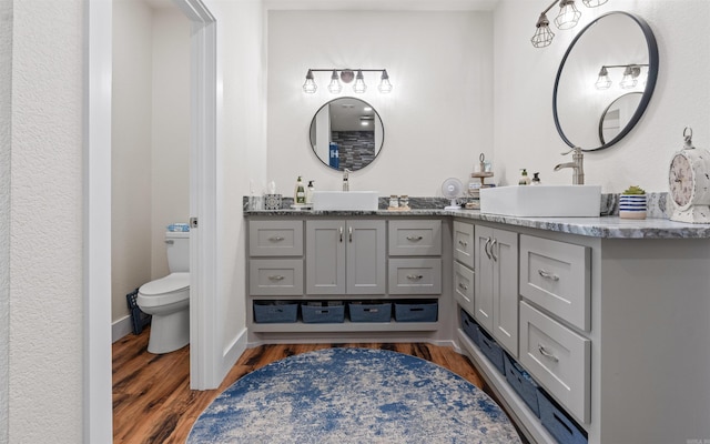 bathroom with toilet, vanity, baseboards, and wood finished floors