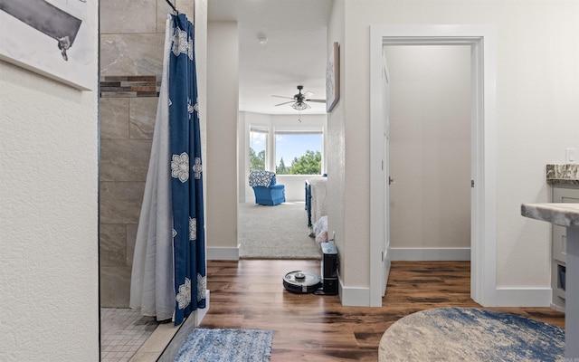 bathroom featuring ceiling fan, wood finished floors, baseboards, and tiled shower