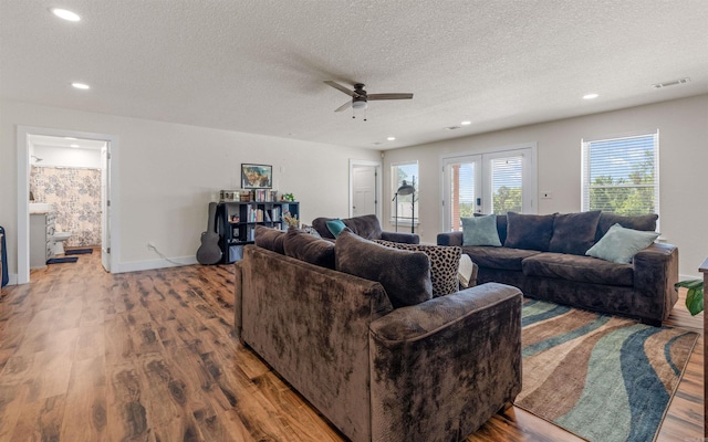 living area featuring baseboards, a textured ceiling, a ceiling fan, and wood finished floors