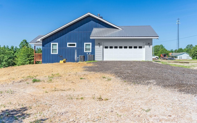 view of side of property with dirt driveway, an attached garage, central AC, and metal roof