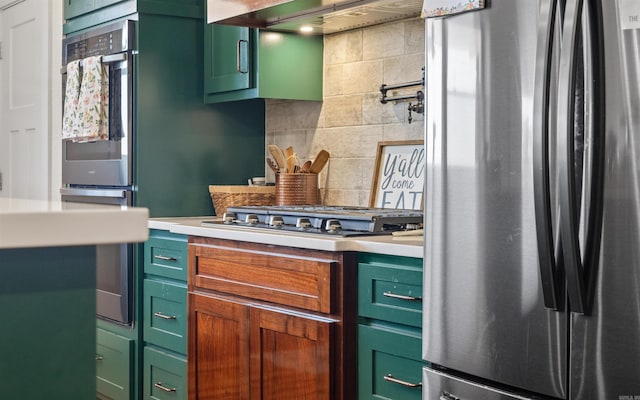 kitchen with ventilation hood, decorative backsplash, light countertops, appliances with stainless steel finishes, and green cabinets