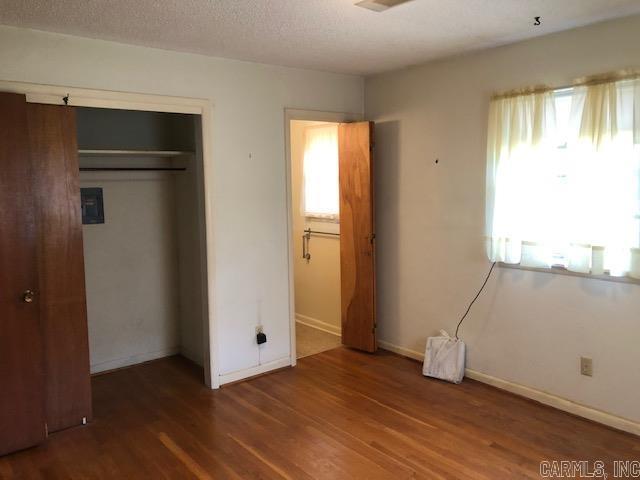 unfurnished bedroom featuring a closet, baseboards, a textured ceiling, and wood finished floors