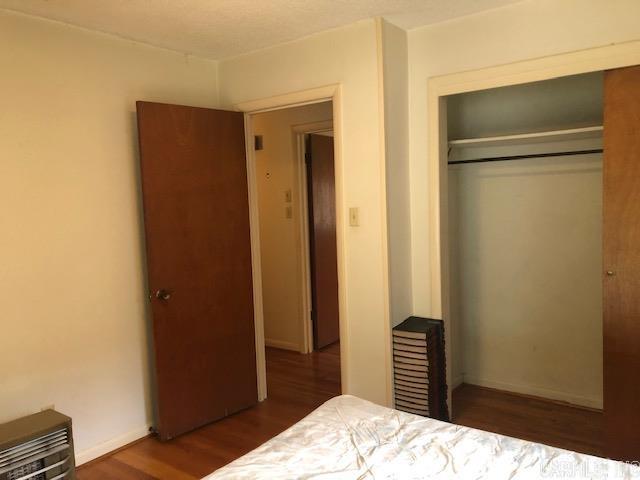 bedroom with a closet, heating unit, and wood finished floors