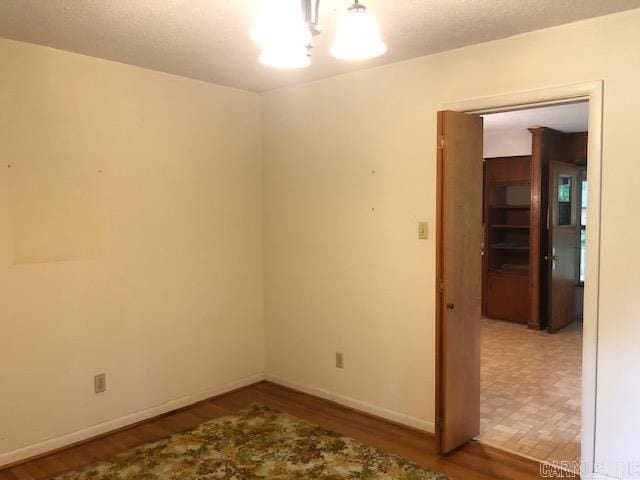 spare room with baseboards, a notable chandelier, and wood finished floors