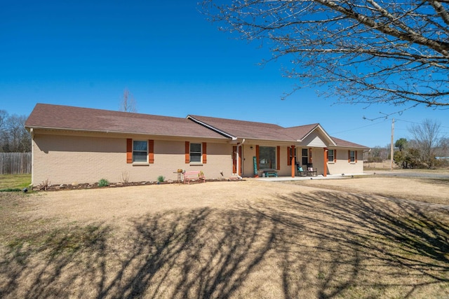 view of front facade featuring brick siding, covered porch, a front yard, and fence