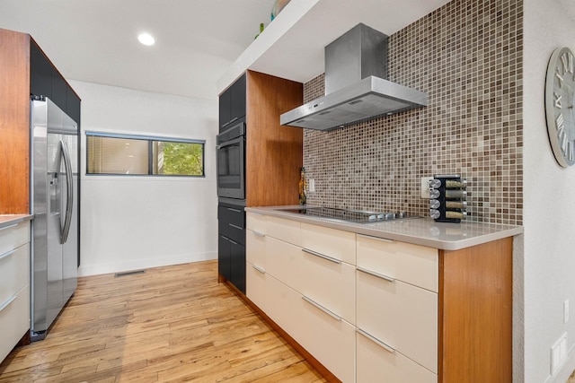 kitchen featuring stainless steel refrigerator with ice dispenser, wall oven, electric cooktop, wall chimney range hood, and tasteful backsplash