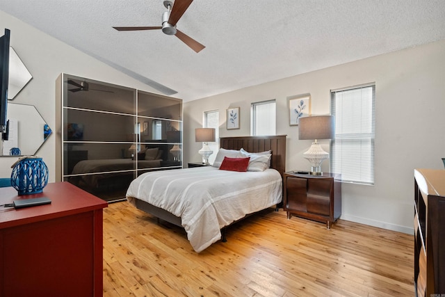 bedroom with light wood-type flooring, a textured ceiling, ceiling fan, and vaulted ceiling