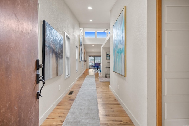 hall featuring a textured wall, recessed lighting, baseboards, and light wood finished floors