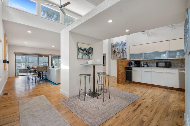 kitchen with visible vents, beverage cooler, backsplash, black microwave, and light wood finished floors