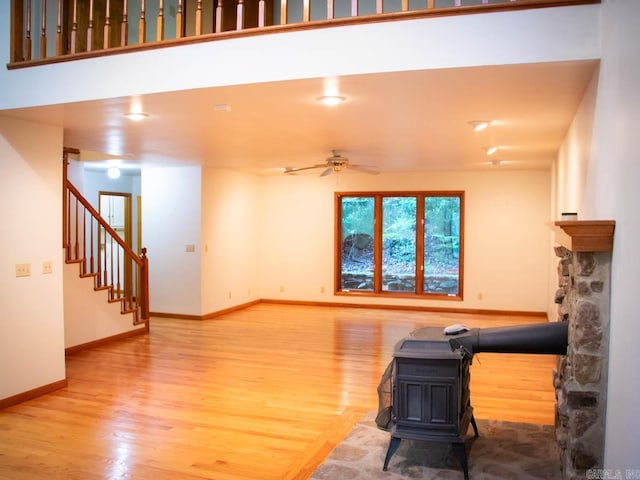 unfurnished living room with stairway, a ceiling fan, wood finished floors, baseboards, and a wood stove