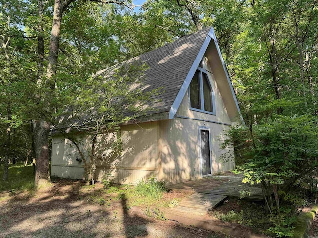 view of side of property featuring an outbuilding and roof with shingles