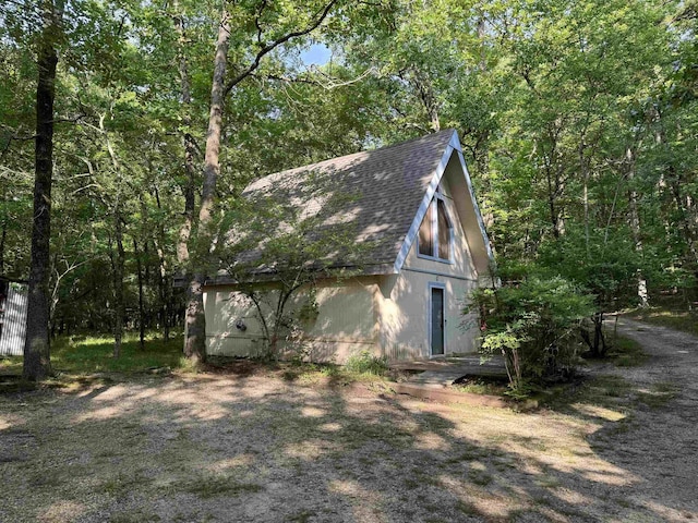 view of home's exterior with an outdoor structure, a barn, roof with shingles, and stucco siding