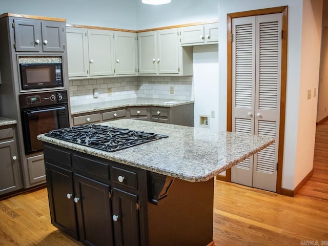 kitchen featuring black appliances, light stone counters, light wood-style floors, and tasteful backsplash