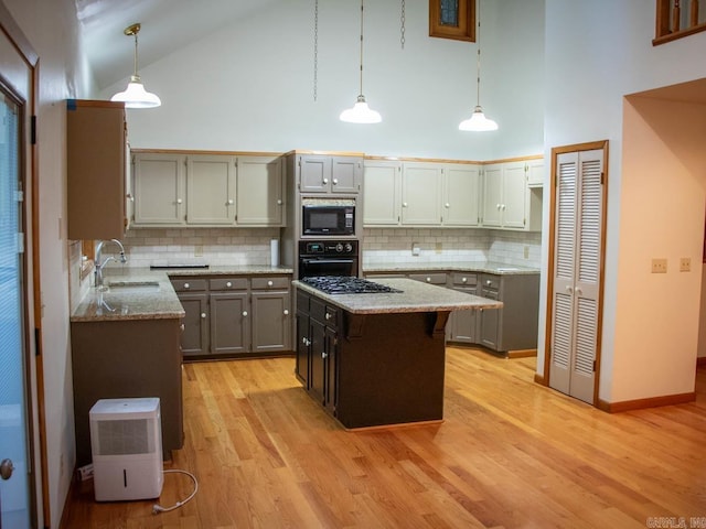 kitchen with high vaulted ceiling, black appliances, light wood-style flooring, a sink, and light stone counters