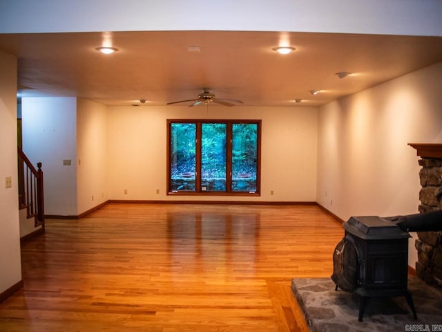living area featuring light wood-type flooring, a ceiling fan, stairway, baseboards, and a wood stove
