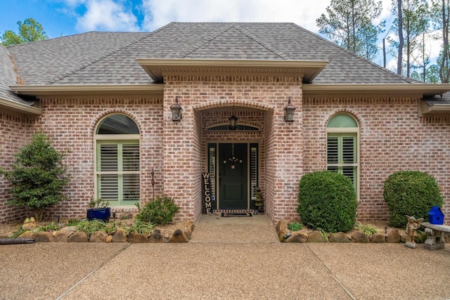 view of exterior entry featuring brick siding and roof with shingles