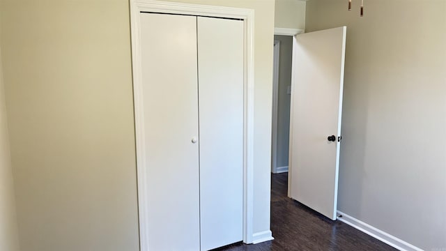 unfurnished bedroom featuring dark wood-style floors, baseboards, and a closet