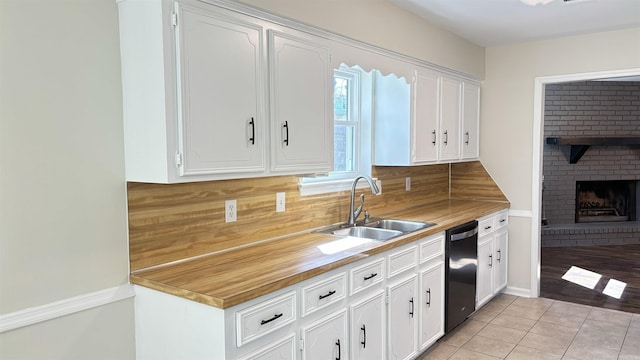 kitchen featuring a brick fireplace, black dishwasher, light tile patterned floors, white cabinets, and a sink