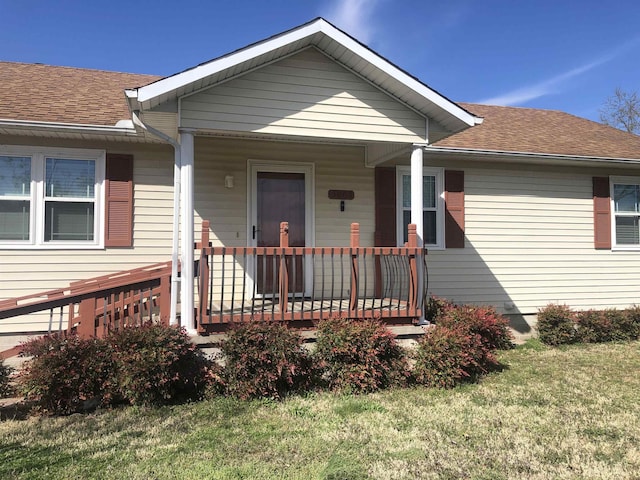 view of front of home featuring covered porch, a front lawn, and a shingled roof