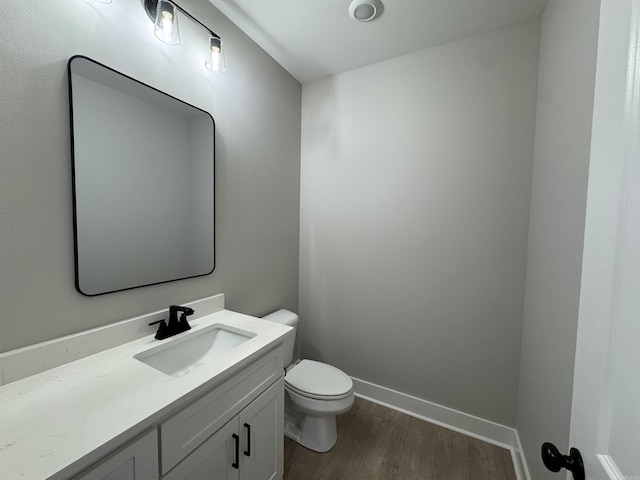 half bath with vanity, toilet, wood finished floors, and baseboards