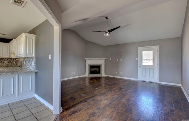 unfurnished living room featuring wood finished floors, a ceiling fan, visible vents, a high end fireplace, and vaulted ceiling