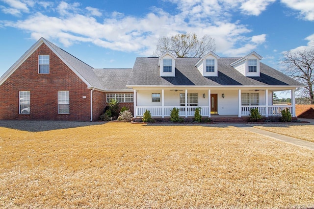 cape cod house featuring brick siding, covered porch, a front lawn, and roof with shingles