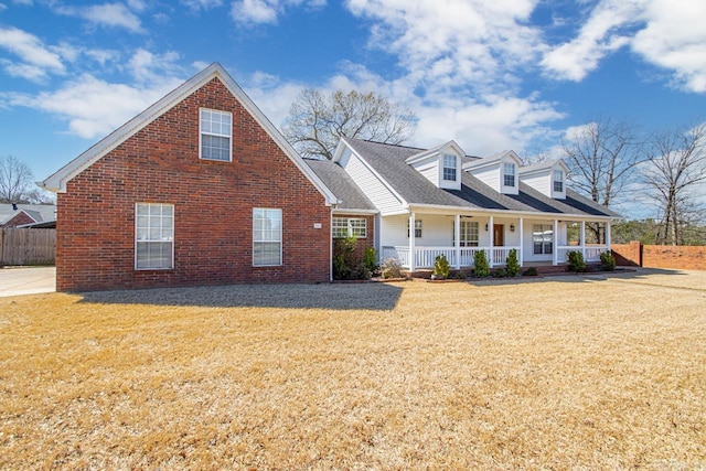 cape cod house with a porch, brick siding, a front yard, and roof with shingles