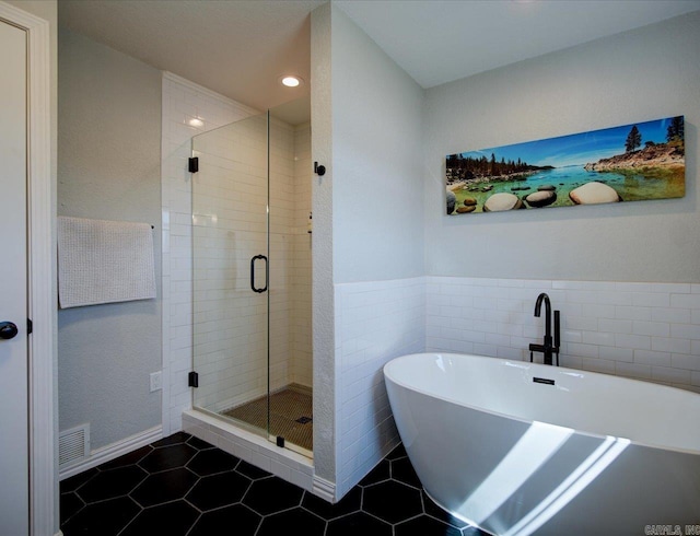 full bathroom featuring visible vents, a shower stall, a freestanding tub, tile patterned floors, and tile walls
