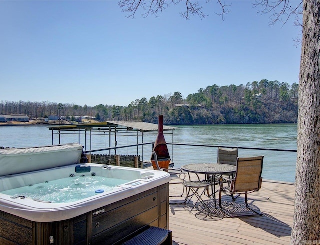 dock area with a wooded view, a water view, and a hot tub
