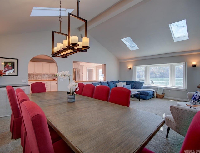 carpeted dining area with arched walkways, a notable chandelier, beam ceiling, and a skylight