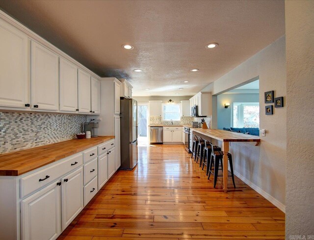 kitchen with tasteful backsplash, butcher block countertops, light wood-type flooring, appliances with stainless steel finishes, and white cabinetry