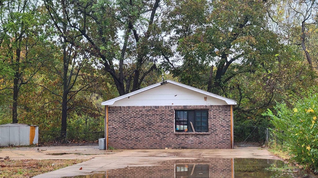 view of side of home with an outdoor structure, a forest view, and brick siding