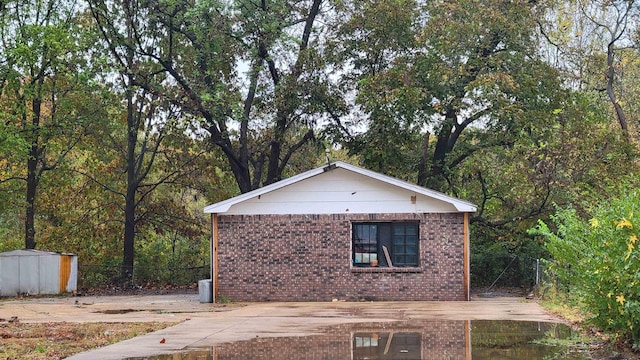 view of side of home with an outdoor structure, a forest view, and brick siding