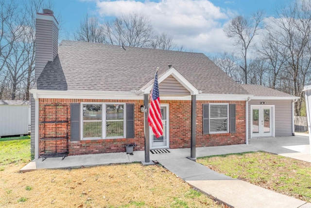 view of front of property featuring a front lawn, french doors, brick siding, and a chimney