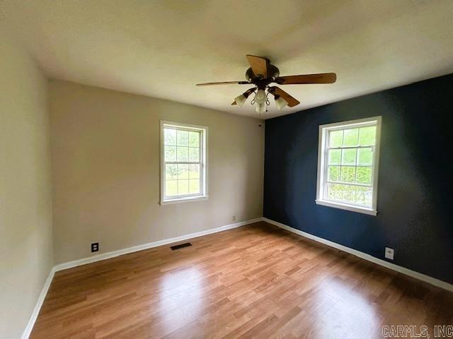 empty room with a ceiling fan, visible vents, wood finished floors, and baseboards