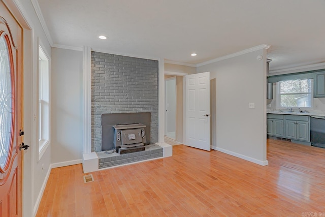 unfurnished living room featuring visible vents, light wood-style flooring, a wood stove, and ornamental molding