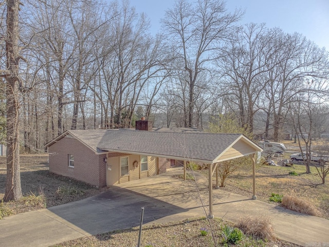 view of front of house with an attached carport, driveway, a chimney, and roof with shingles