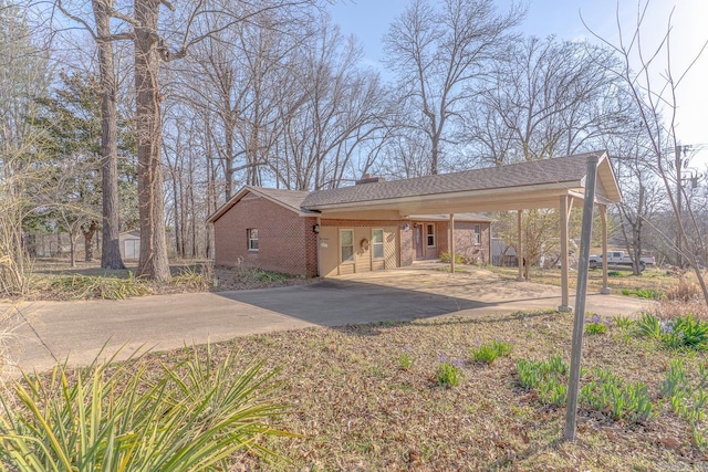 view of front facade with brick siding, a chimney, concrete driveway, and a carport