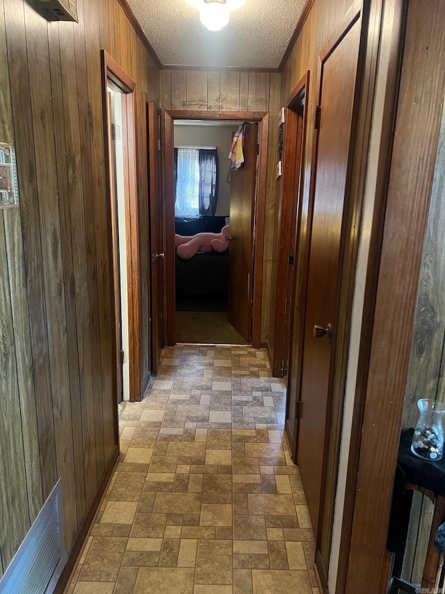 corridor featuring wooden walls, a textured ceiling, brick patterned floor, visible vents, and ornamental molding