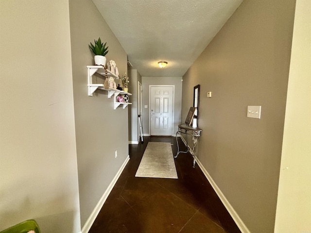 hallway with dark tile patterned floors, a textured ceiling, and baseboards