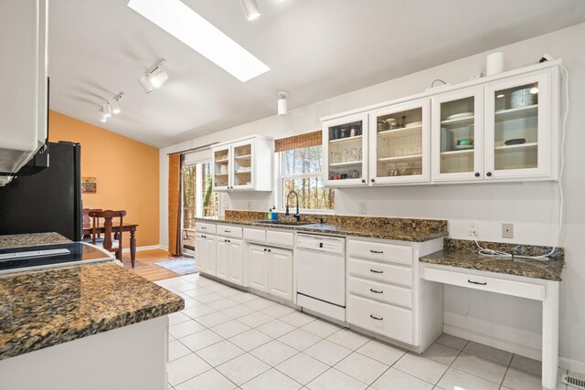 kitchen featuring vaulted ceiling with skylight, freestanding refrigerator, white dishwasher, white cabinets, and a sink